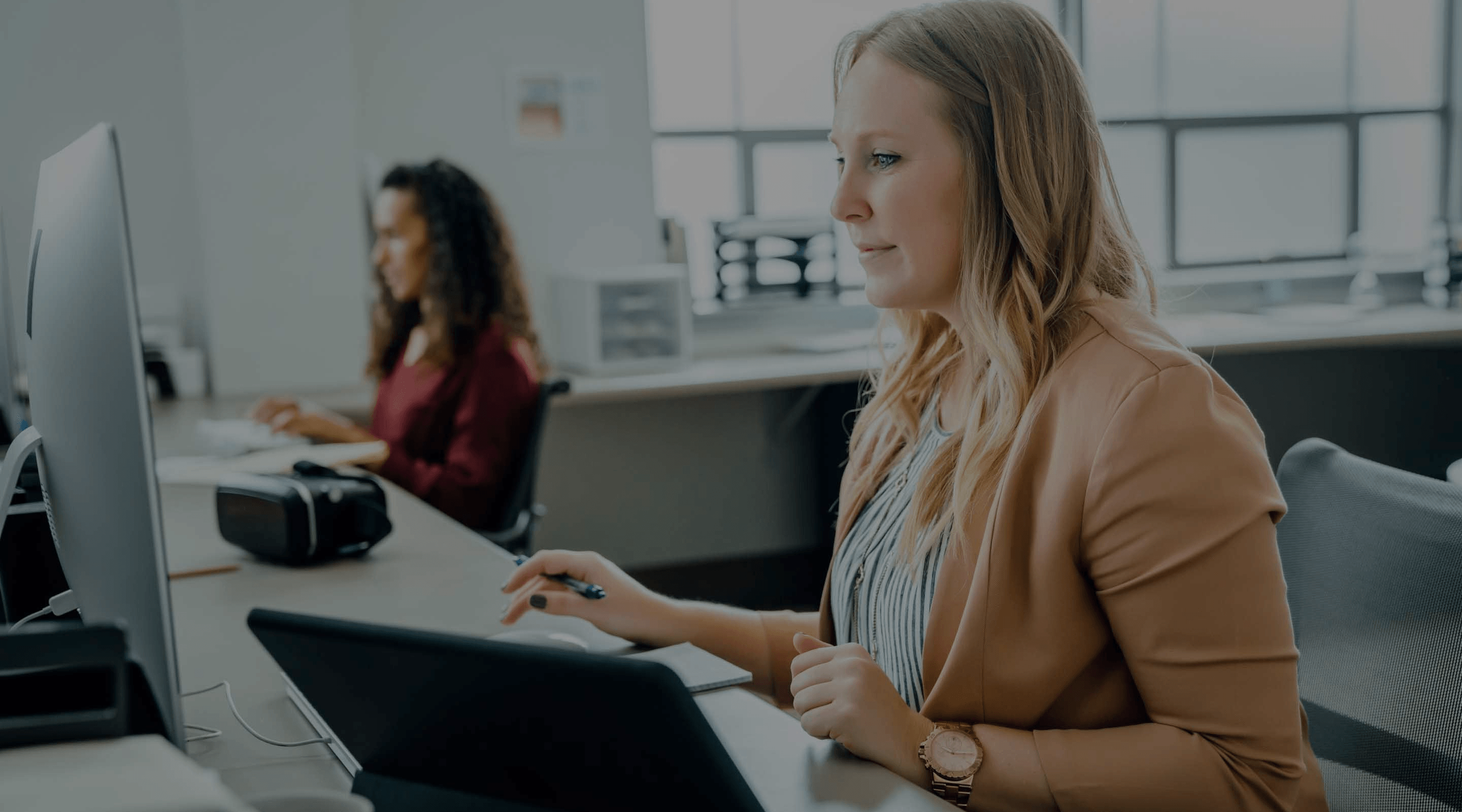 Image of two people working in an office with an open floor plan, viewing their computer screens.
