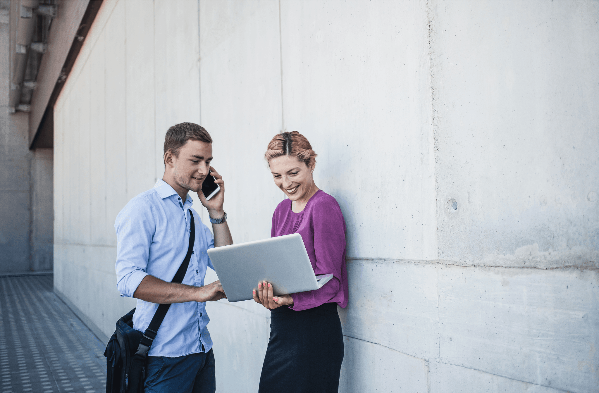 Image of two people outside of their office using a laptop and a mobile phone.