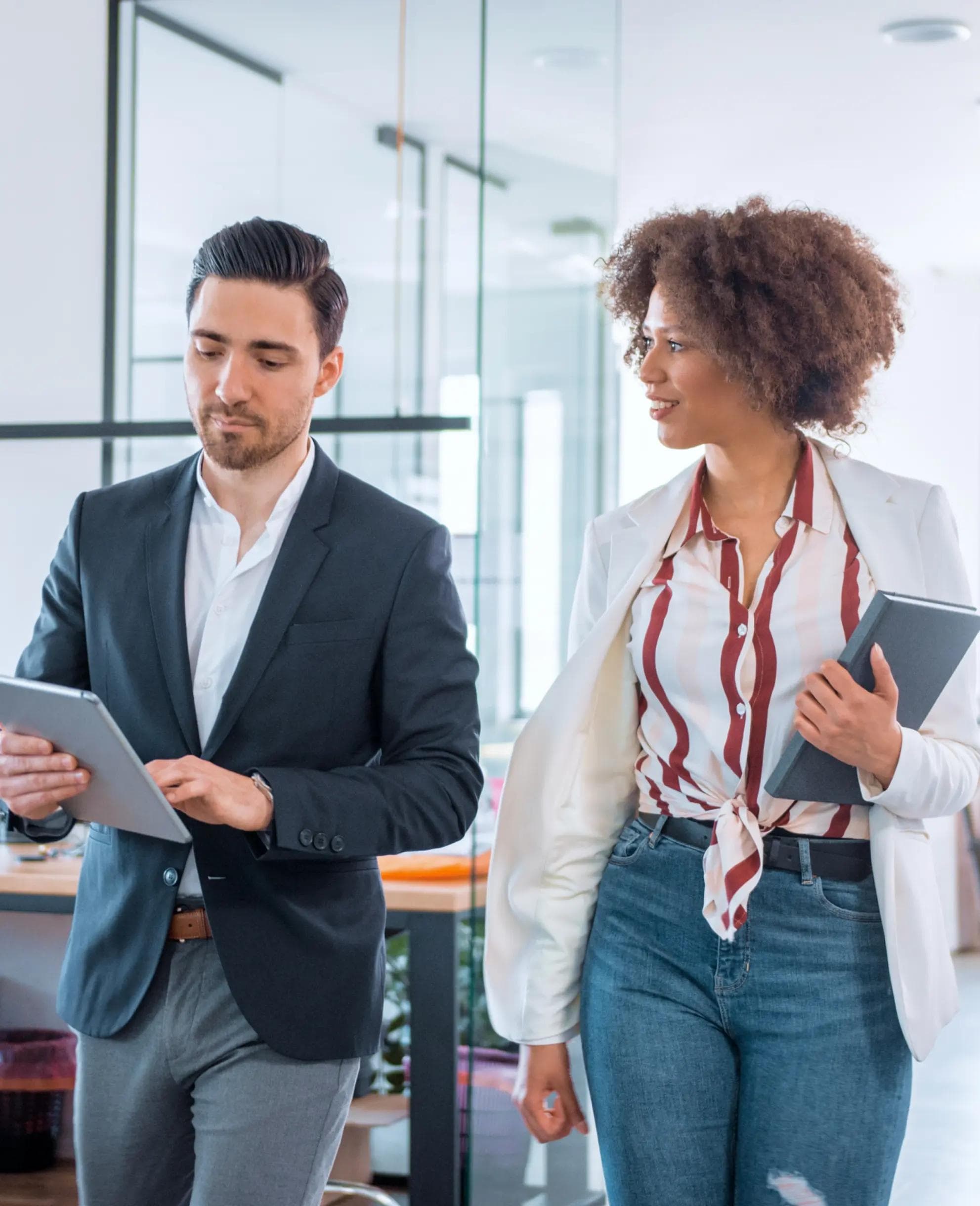 Two people walking through office with tablet and notebook in hand.