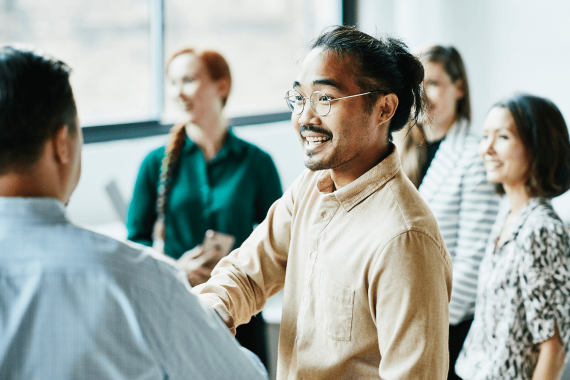 A man shakes hands with another man in front of a group of people.
