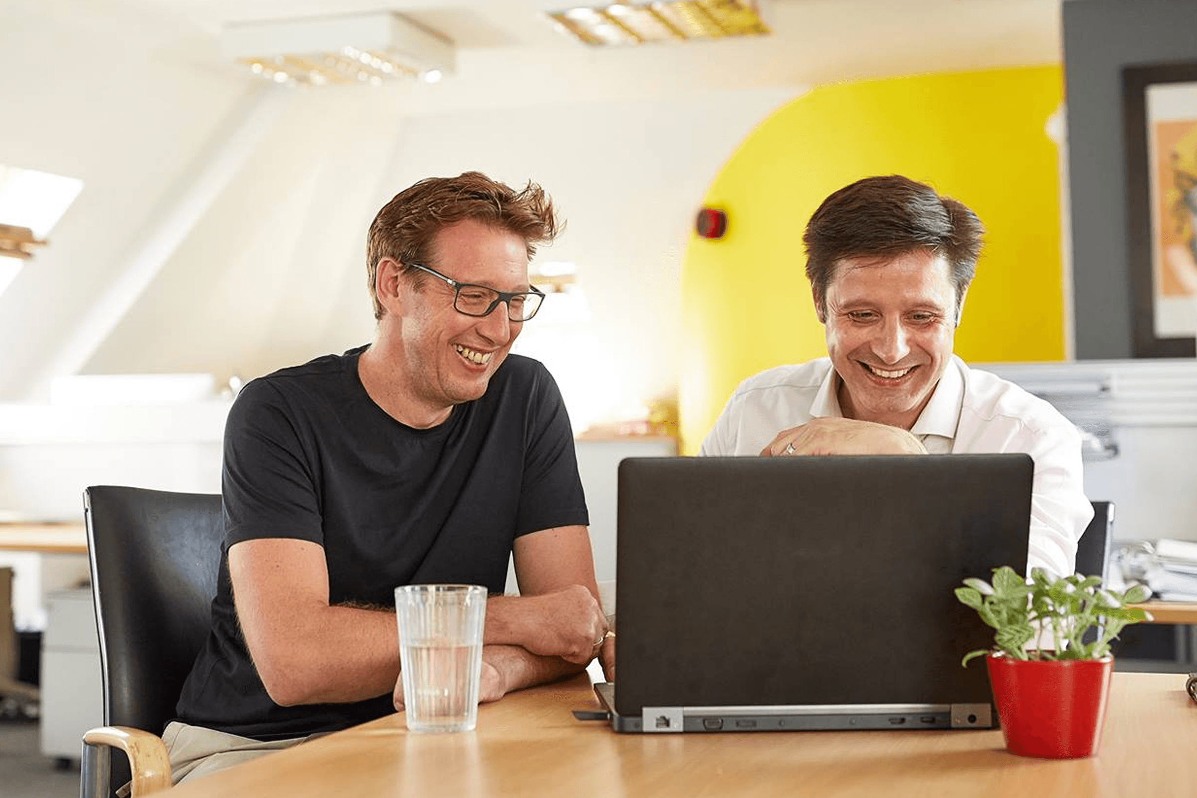 Two men laughing together at a laptop.